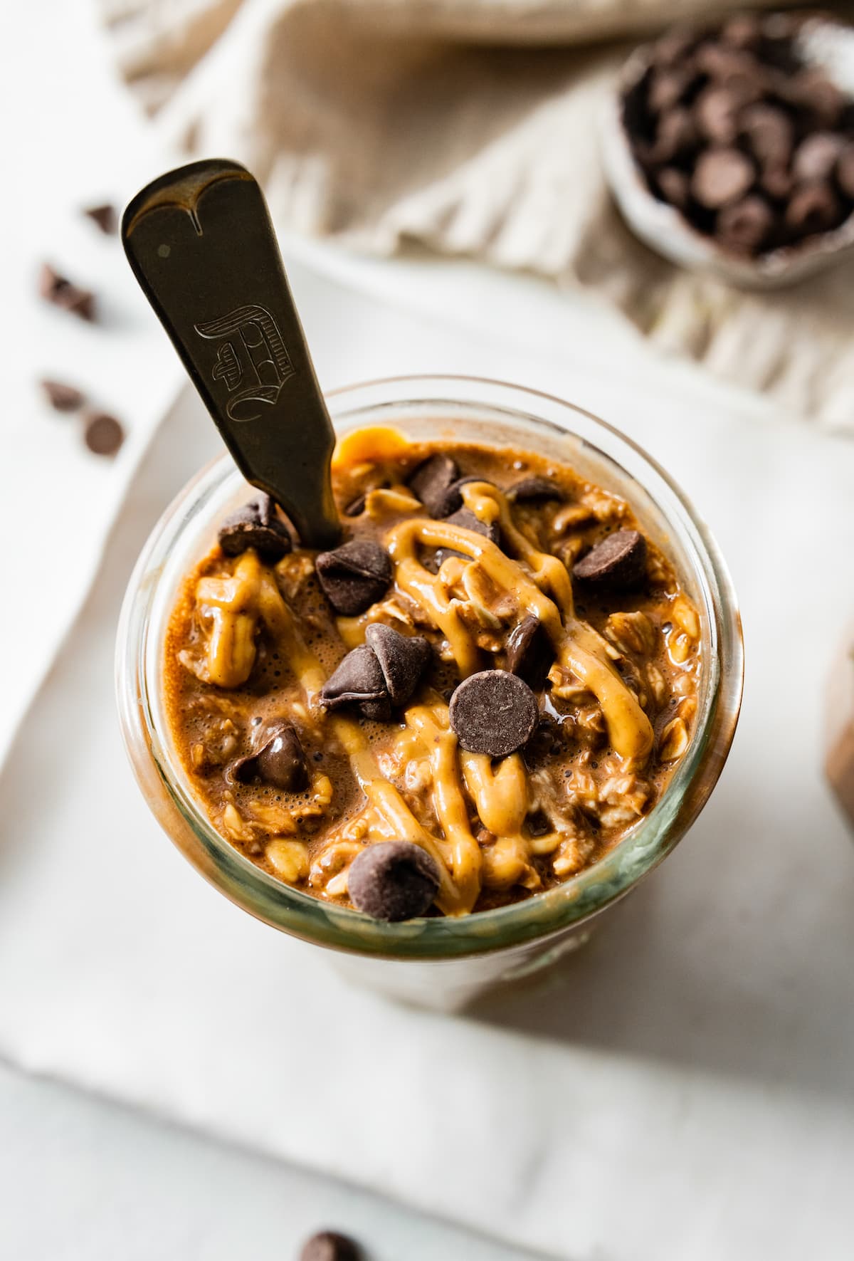 The chocolate overnight oats topped with chocolate chips and a drizzle of peanut butter and served with a spoon.