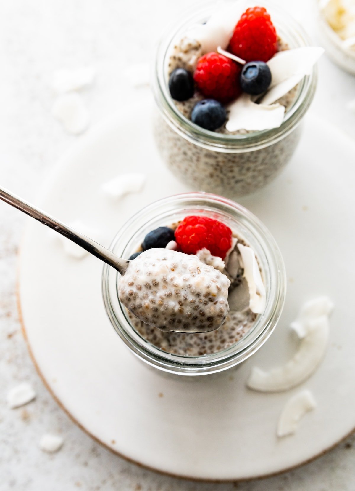 A spoon holding a bite-size portion of coconut chia pudding over a cup of the pudding.