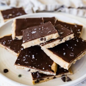 Cut protein cookie dough bark topped with flaked sea salt angled on a plate.