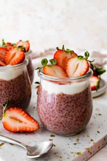 Two glass cups of strawberry chia pudding topped with fresh strawberries.