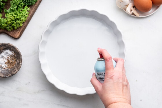 A woman's hand spraying a pie plate with cooking spray.