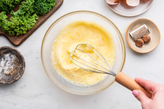 A woman's hand whisking the eggs for the crustless quiche.