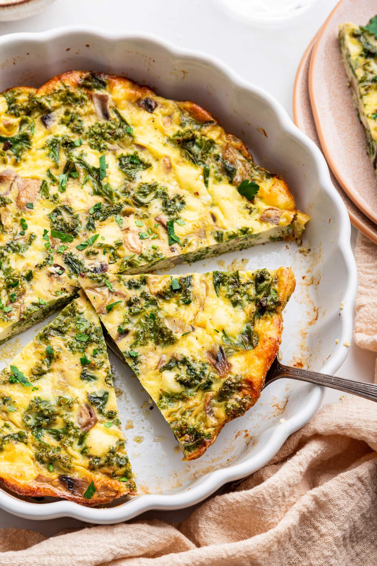 A slice of a crustless quiche being served on a spatula from a pie plate.