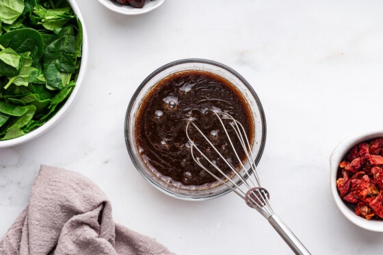 A dressing in a small glass bowl with a whisk.