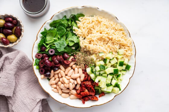 A large bowl full of ingredients used for a mediterranean orzo salad.