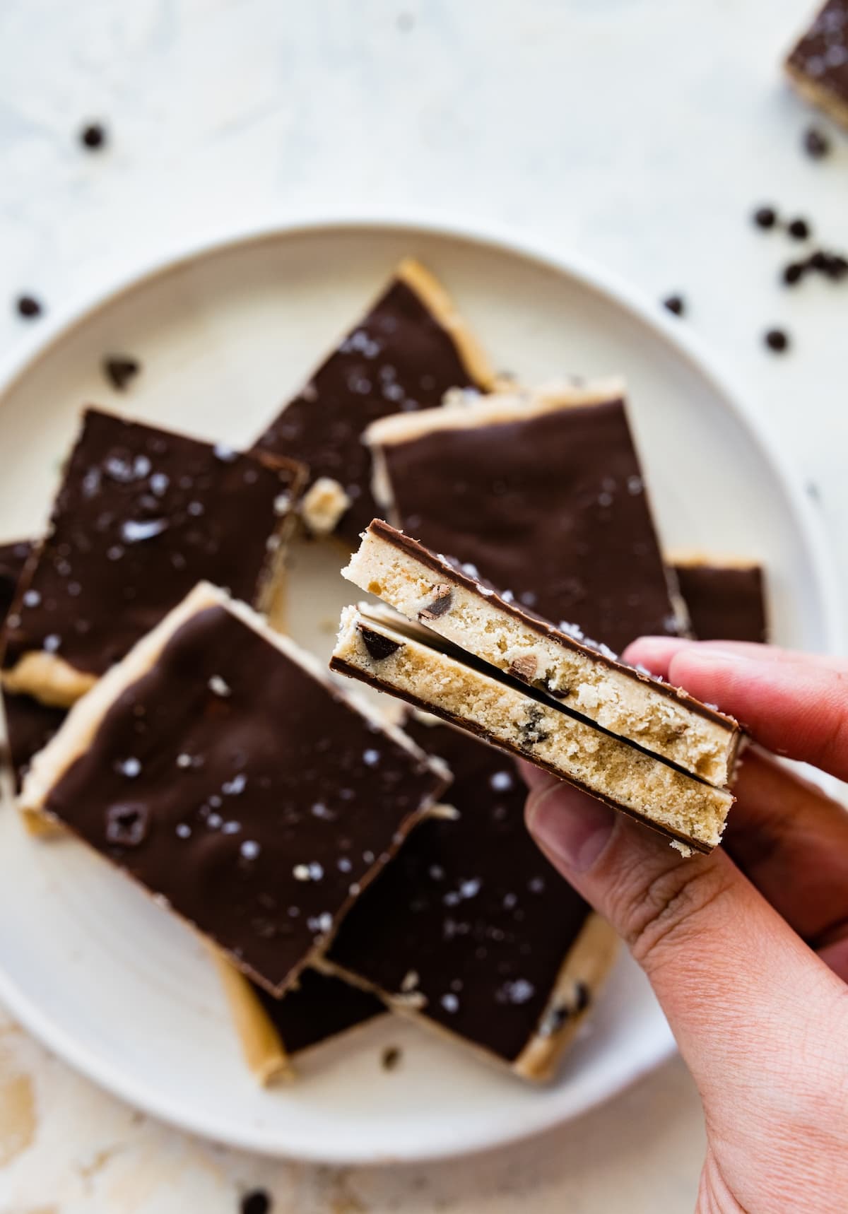 A woman's hand holding two pieces of protein cookie dough bark.