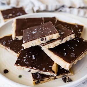 Cut protein cookie dough bark topped with flaked sea salt angled on a plate.