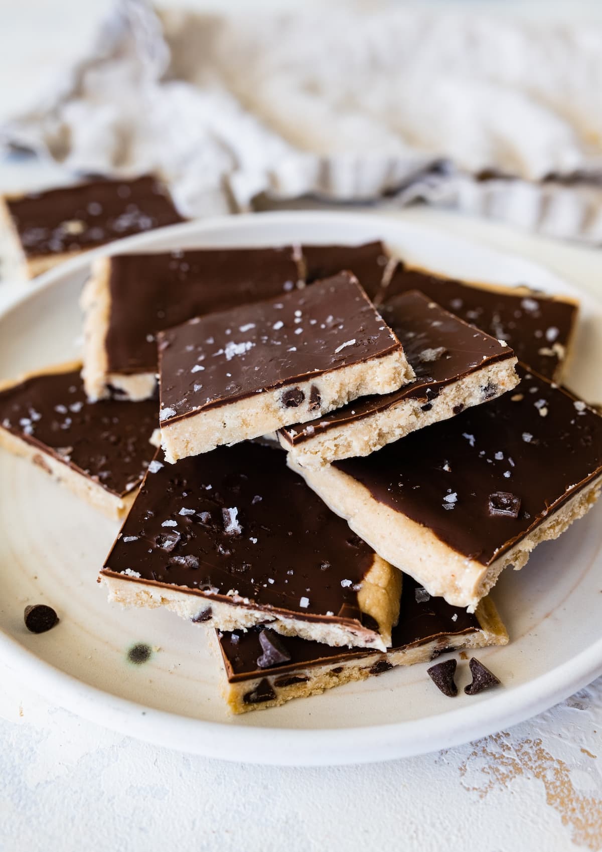 Cut protein cookie dough bark topped with flaked sea salt angled on a plate.