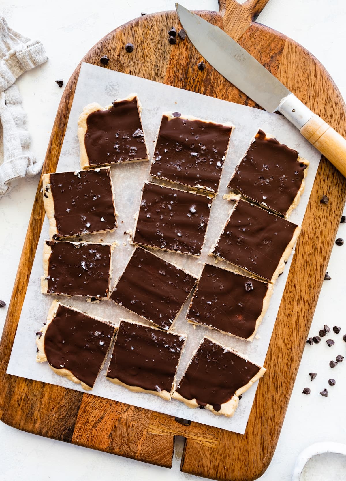 12 pieces of protein cookie dough bark topped with flaked sea salt on a cutting board.