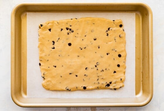 The protein cookie dough bark dough spread into a rectangle on a baking sheet lined with parchment paper.