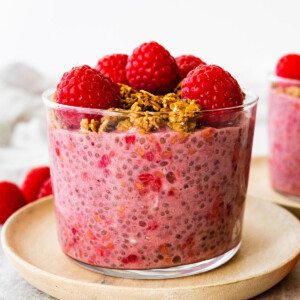 A raspberry chia pudding in a glass cup, topped with fresh raspberries and granola.