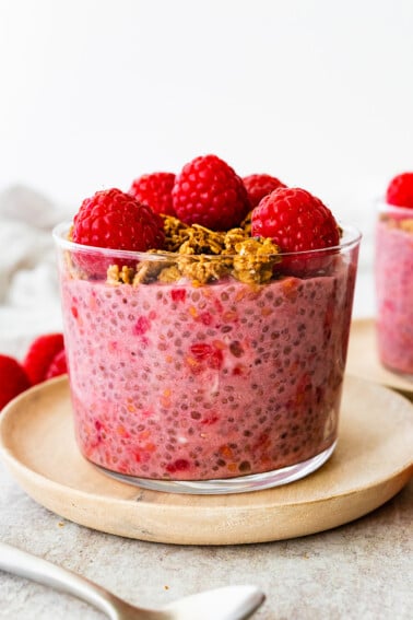 A raspberry chia pudding in a glass cup, topped with fresh raspberries and granola.