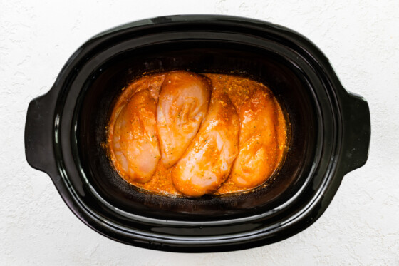 Four chicken breasts seasoned in buffalo sauce in a slow cooker.