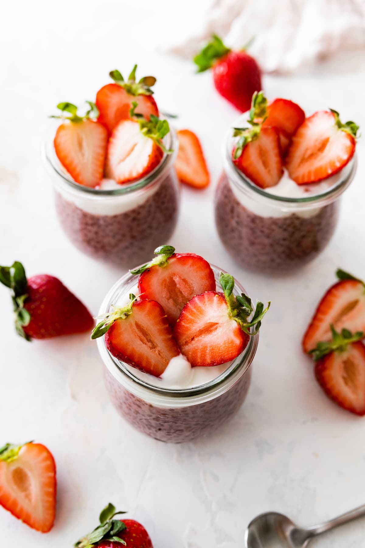 Three glass cups of strawberry chia pudding topped with fresh strawberries.