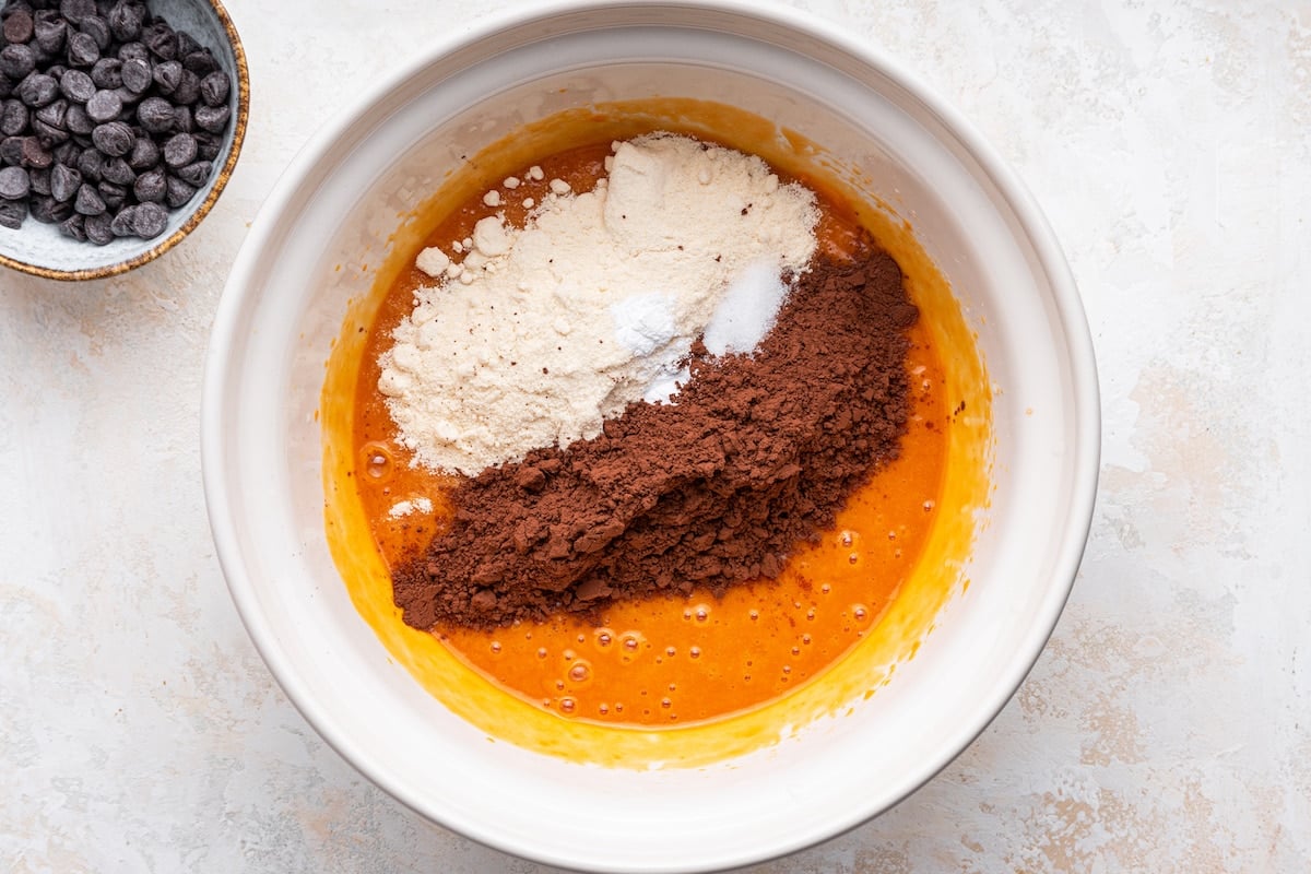 Cocoa powder, coconut flour, and baking soda added to the wet ingredients for sweet potato brownies.
