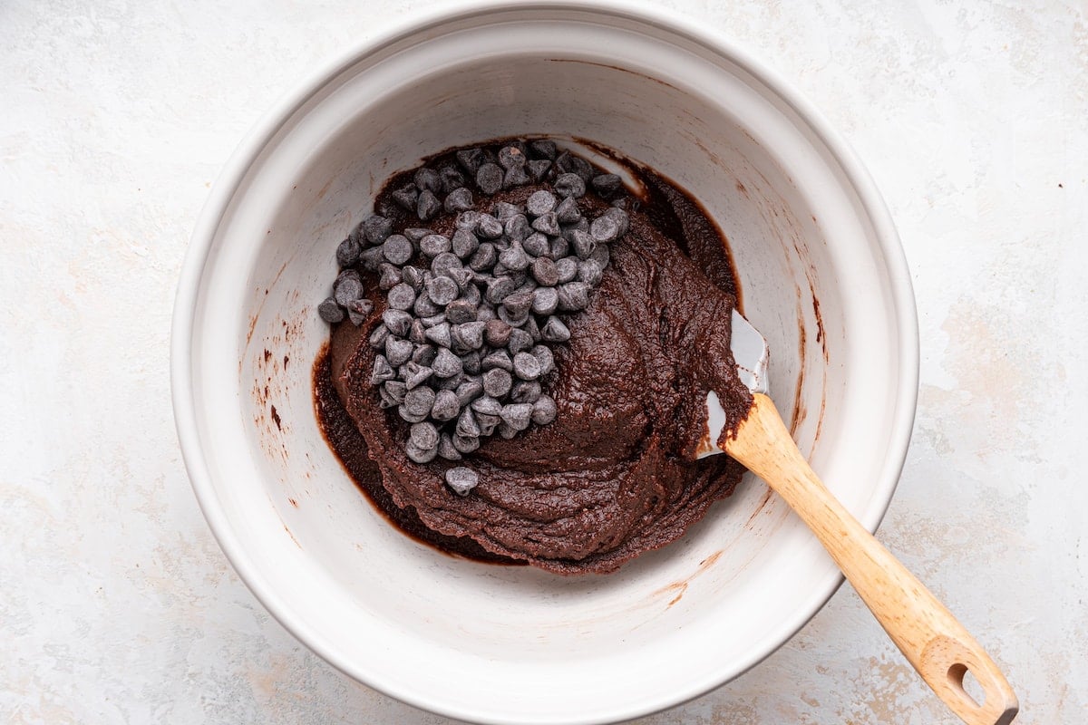 Sweet potato brownie batter in a large bowl with chocolate chips and a silicone spatula.