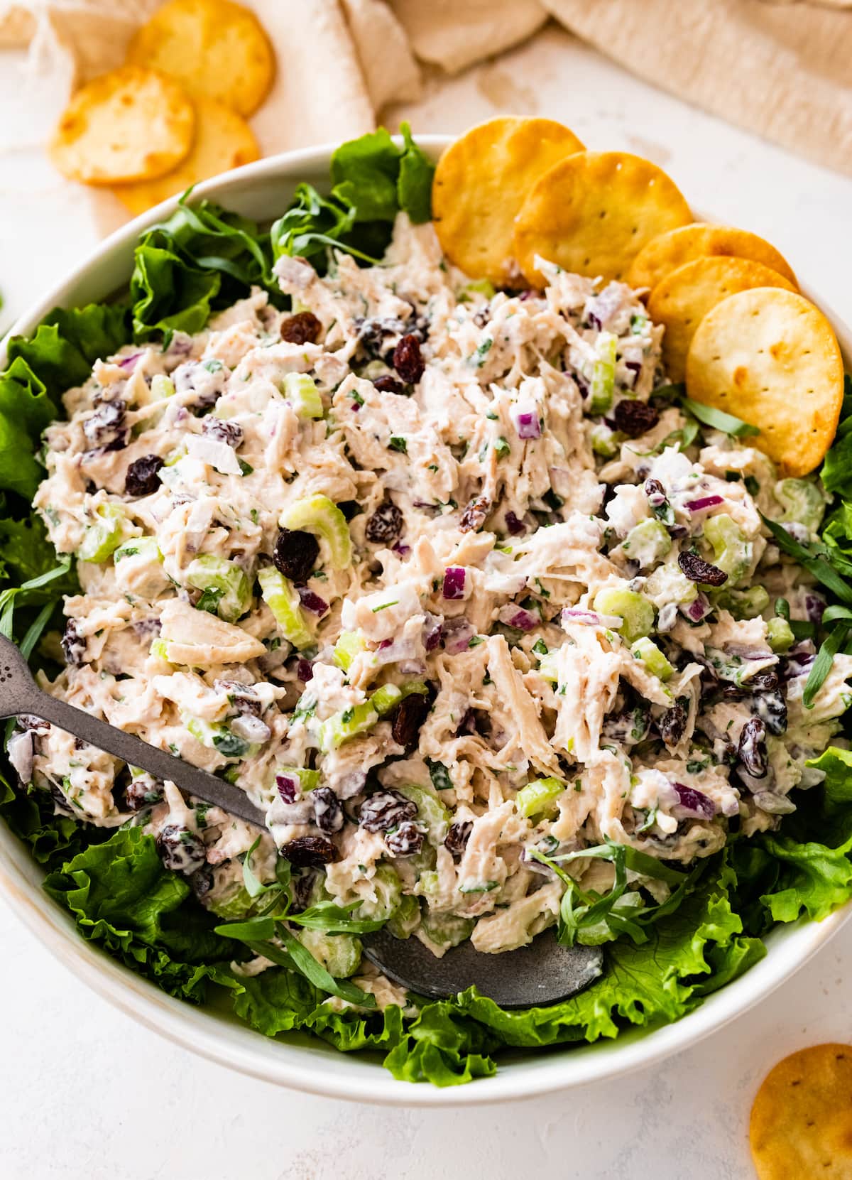 Tarragon chicken salad in a white serving bowl served on top of a bed of greens with crackers.