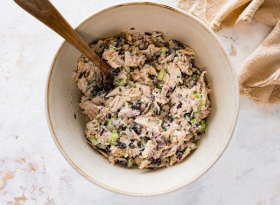 Mixed tarragon chicken salad in a ceramic mixing bowl with a wooden spoon.