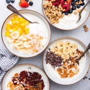 Four yogurt bowls served in white bowls with spoons.