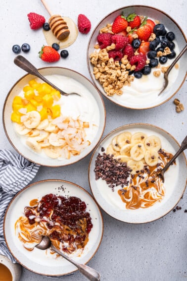 Four yogurt bowls served in white bowls with spoons.