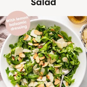 Arugula salad in a bowl with a spoon and topped with parmesan and almonds.