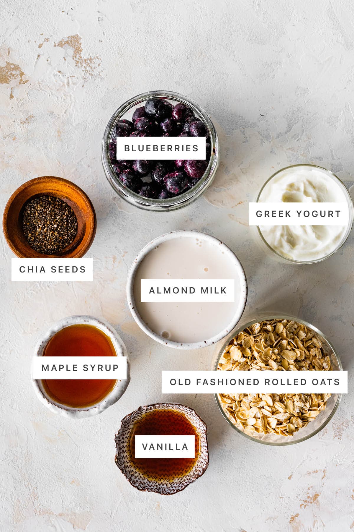 Ingredients measured out to make Blueberry Overnight Oats: blueberries, chia seeds, almond milk, Greek yogurt, maple syrup, vanilla and oats.