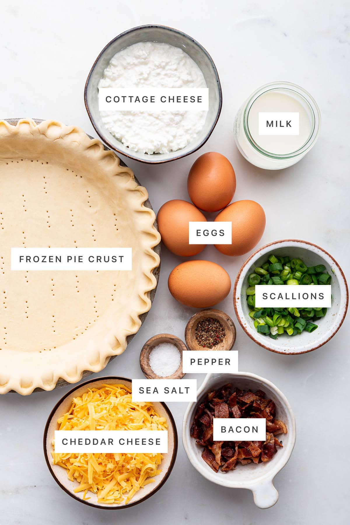 Ingredients measured out to make a Cottage Cheese Quiche: frozen pie crust, cottage cheese, milk, eggs, scallions, pepper, sea salt, cheddar cheese and bacon.