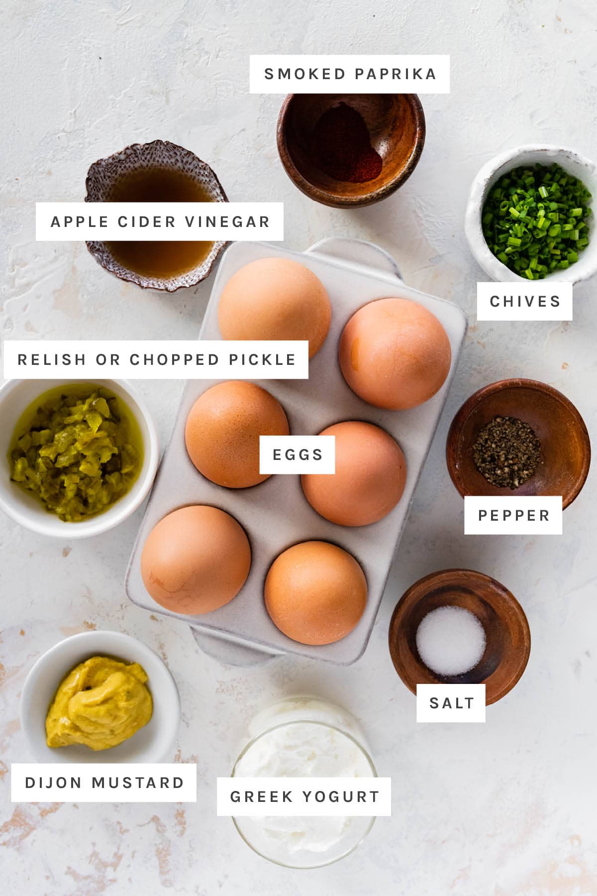 Ingredients measured out to make healthy deviled eggs: apple cider vinegar, smoked paprika, chives, relish, eggs, pepper, dijon, salt and Greek yogurt.
