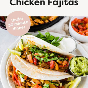 Two tacos with chicken fajitas on a plate served with guacamole, cilantro and sour cream.