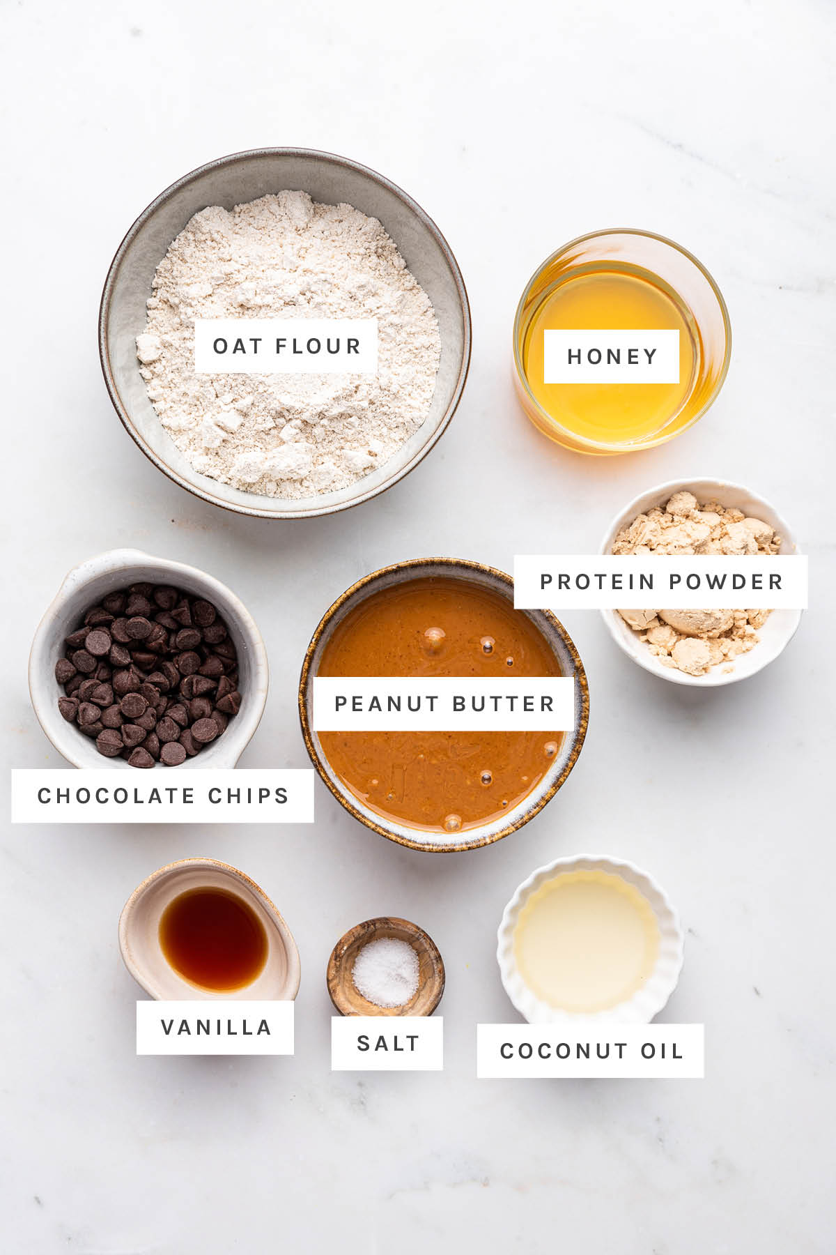Ingredients measured out to make Easy Protein Bars: oat flour, honey, chocolate chips, peanut butter, protein powder, vanilla, salt and coconut oil.