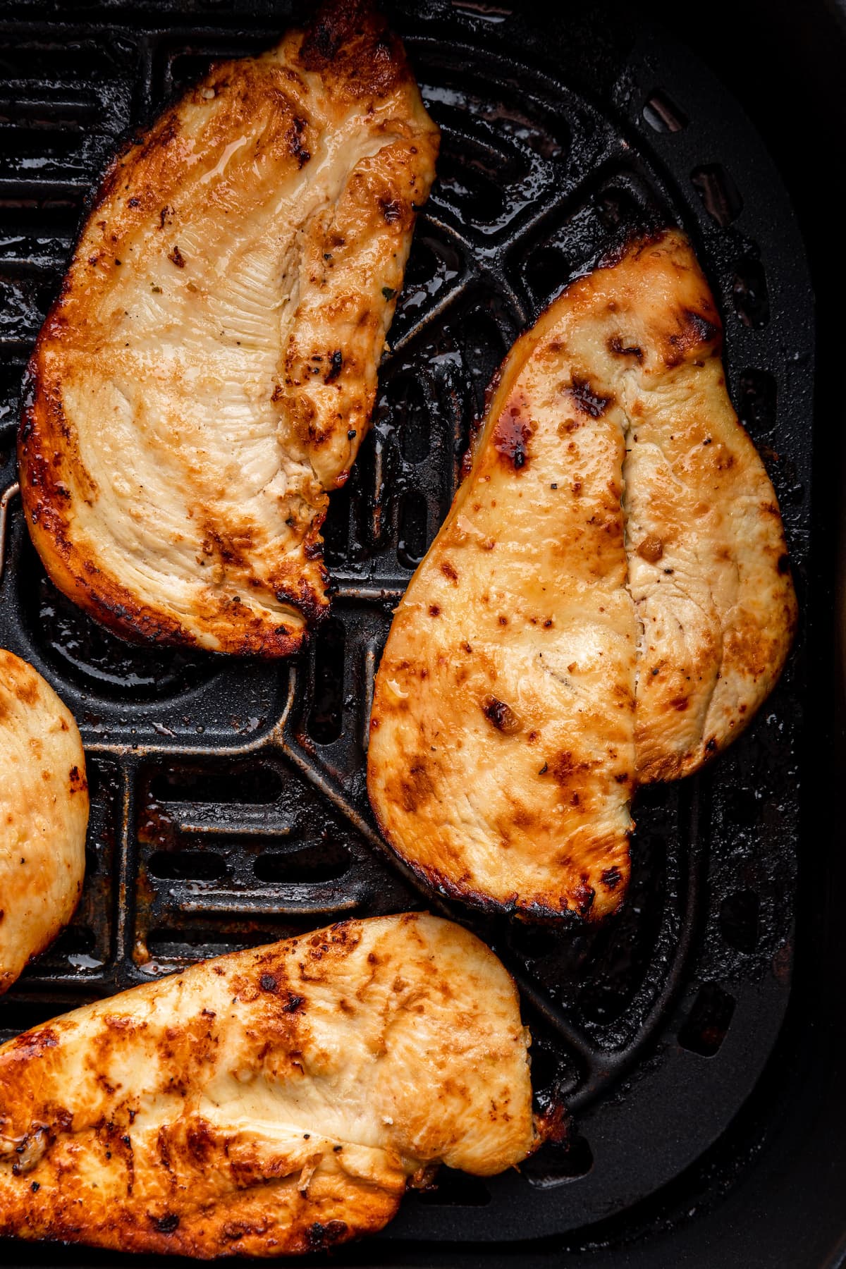 A close up of three cooked chicken cutlets in an air fryer basket.