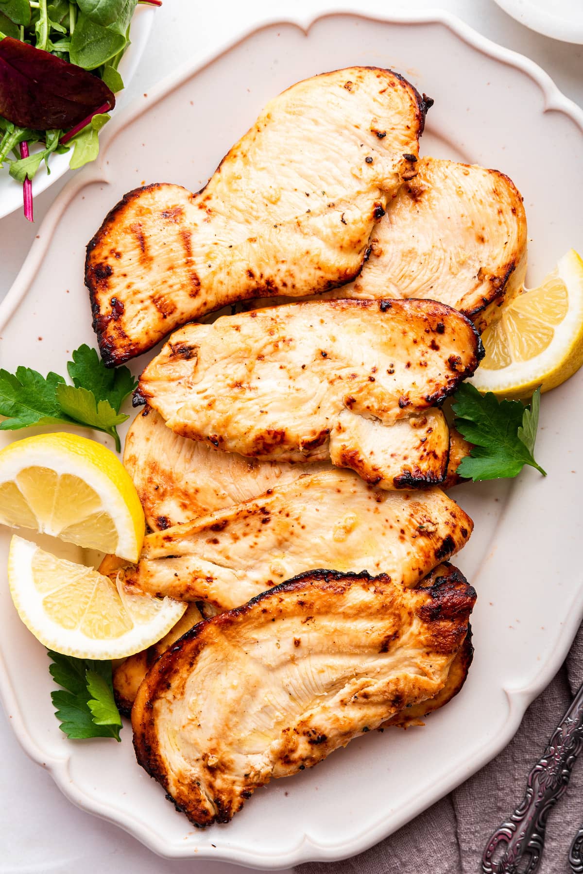 Five cooked chicken cutlets on a serving plate served with lemon wedges and fresh parsley.