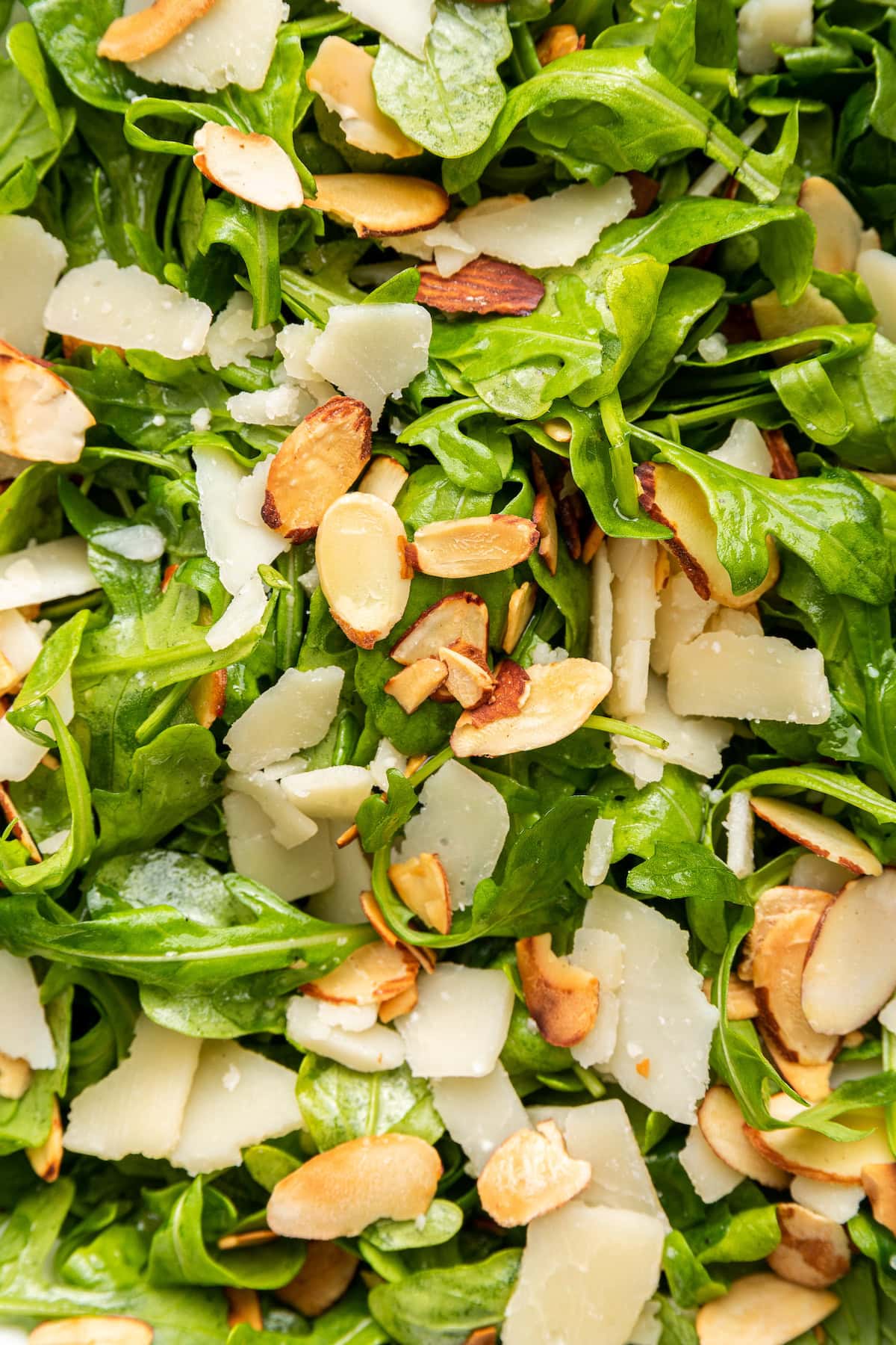 A close up image of an arugula salad topped with parmesan cheese and almonds.