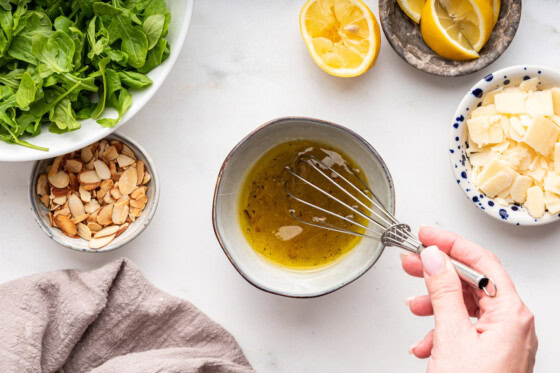 A woman's hand whisking the lemon balsamic dressing for the arugula salad.