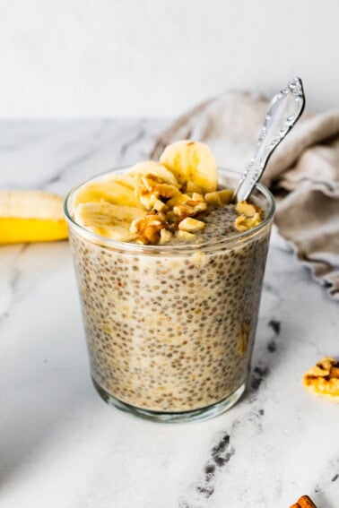 Banana chia pudding in a glass cup, topped with banana slices and walnuts.