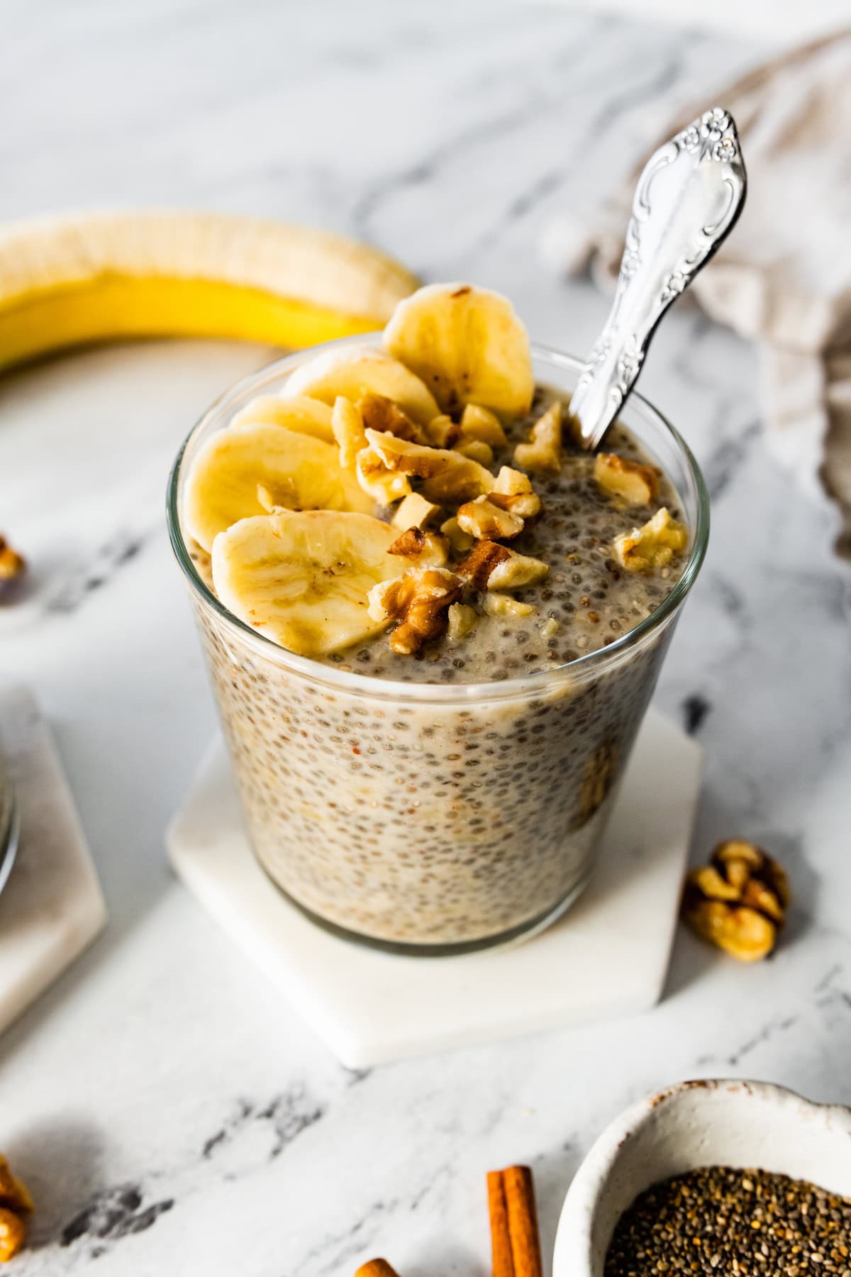 Banana chia pudding in a glass cup, topped with banana slices and walnuts.