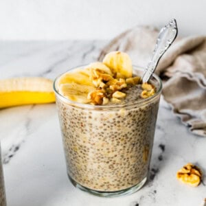 Banana chia pudding in a glass cup, topped with banana slices and walnuts.