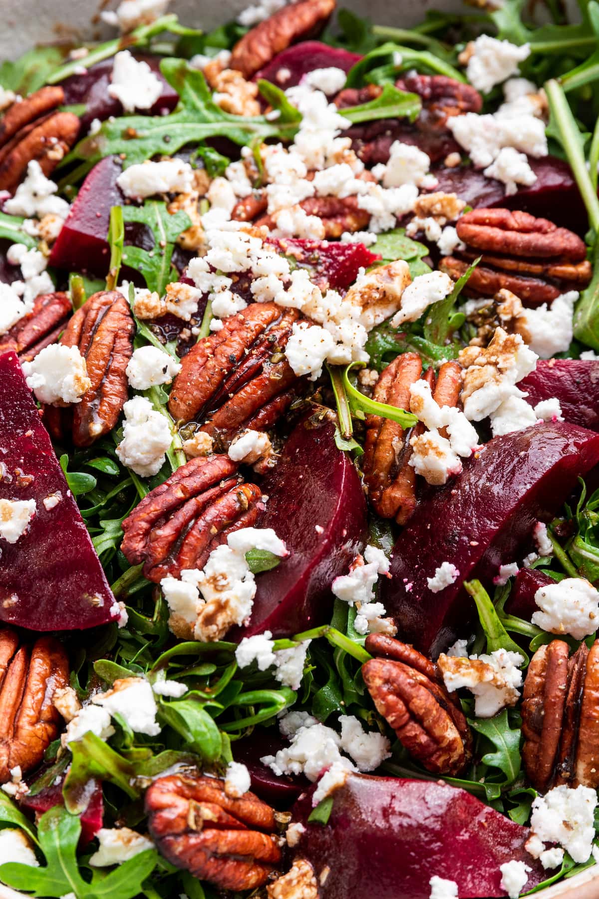 A beet salad with arugula, pecans, and crumbled feta in a bowl.