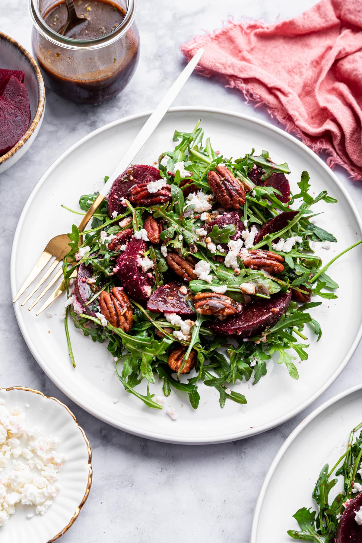A beet salad with arugula, pecans, and crumbled feta on a white plate.