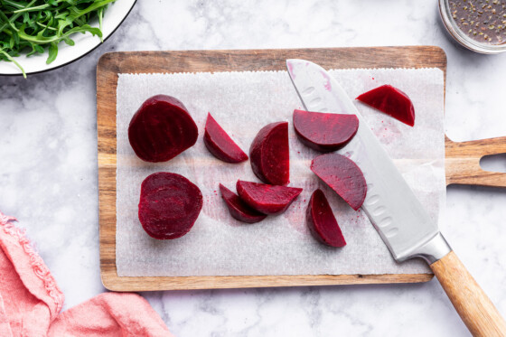 Cut beets on a cutting board with a knife.