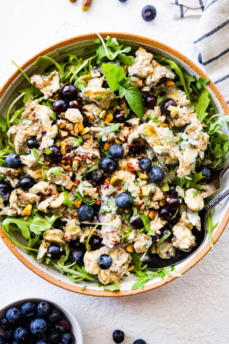 A large bowl of blueberry breakfast salad with scrambled eggs, fresh blueberries, arugula, herbs, and spices.
