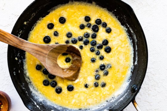 Eggs and blueberries in a skillet with a wooden spoon.