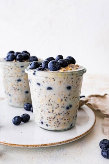 Two glasses of blueberry overnight oats topped with fresh blueberries.