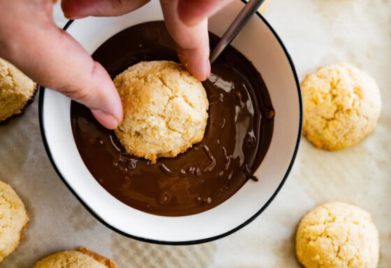 A coconut macaroon being dipped in a small bowl of chocolate.