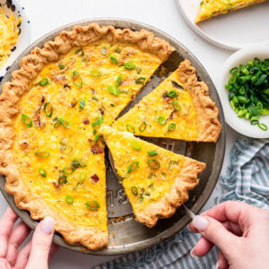 A woman's hand uses a spatula to serve a piece of cottage cheese quiche from the pan.