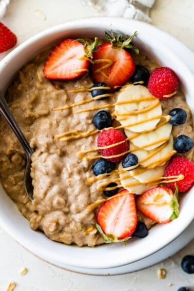 A bowl of protein oatmeal topped with fresh berries, banana slices, and a drizzle of nut butter.