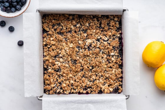 The blueberries topped with the crumble part in a square baking pan for the blueberry crumble bars.