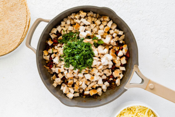 Chicken added to a large skillet with cooked onion, tomato, and corn.