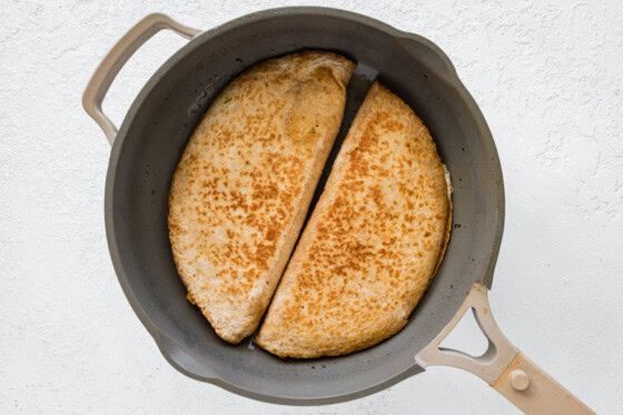 Two chicken quesadillas being cooked in a large skillet.