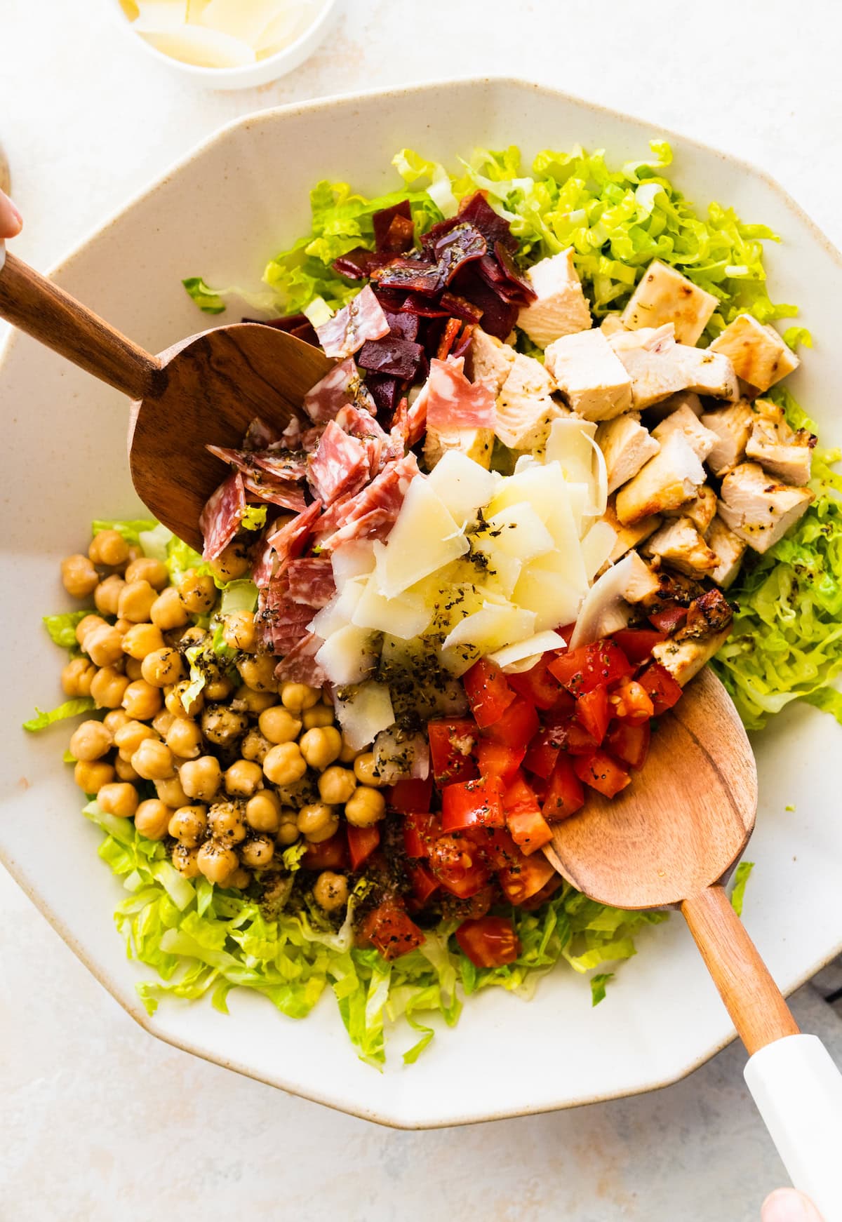 Protein cobb salad in a large salad bowl being mixed with two wooden spoons.